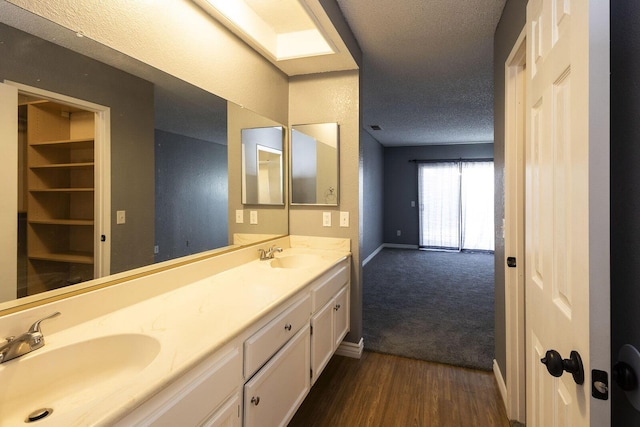 full bath featuring a sink, double vanity, a textured ceiling, and wood finished floors