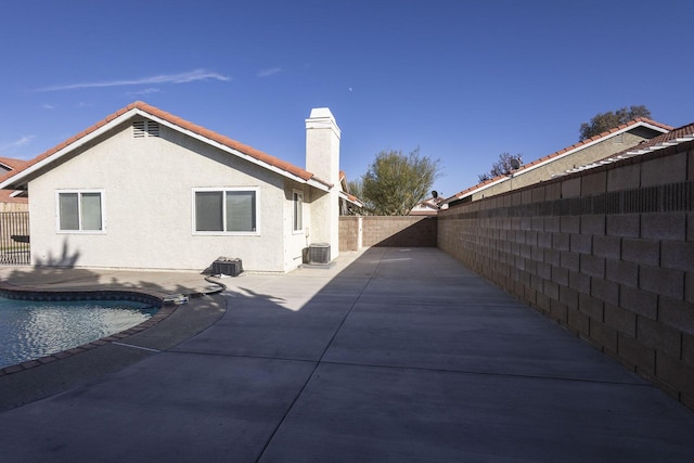 back of property with stucco siding, a fenced backyard, central AC unit, a chimney, and a patio