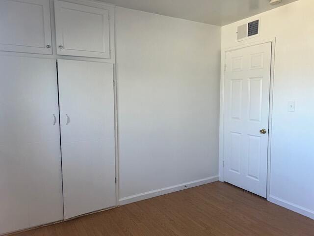 unfurnished bedroom featuring wood finished floors, visible vents, a closet, and baseboards