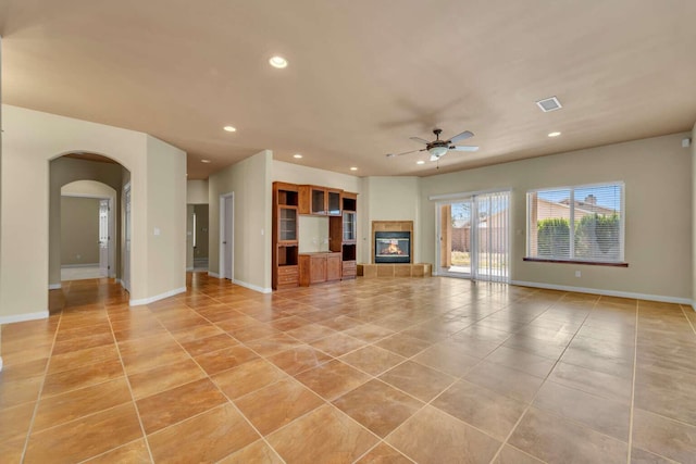 unfurnished living room featuring ceiling fan, a tiled fireplace, recessed lighting, arched walkways, and light tile patterned floors