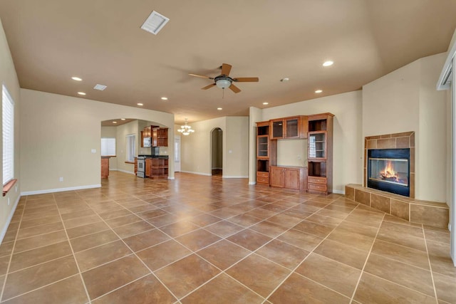 unfurnished living room with tile patterned flooring, recessed lighting, ceiling fan with notable chandelier, arched walkways, and a tile fireplace