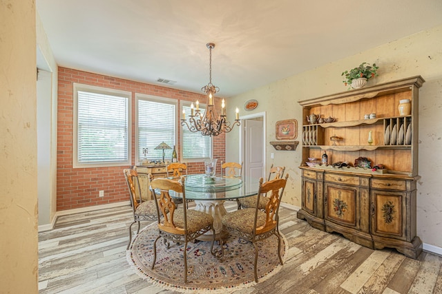 dining area with brick wall, a notable chandelier, and light wood-type flooring