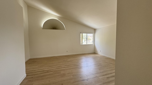 spare room featuring wood finished floors, baseboards, and vaulted ceiling
