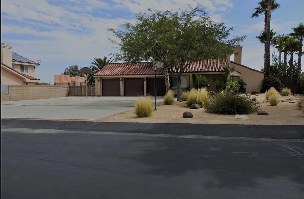 mediterranean / spanish home with stucco siding, driveway, a tile roof, fence, and a garage