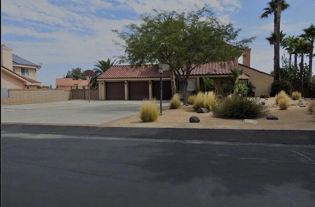 mediterranean / spanish home with stucco siding, driveway, a tile roof, fence, and a garage