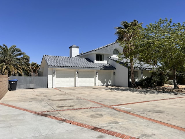 view of side of property with concrete driveway, stucco siding, a chimney, and a tile roof
