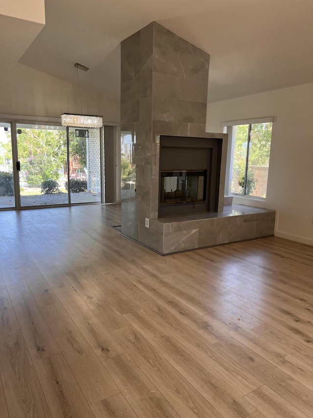 unfurnished living room featuring wood finished floors, high vaulted ceiling, a fireplace, and a notable chandelier