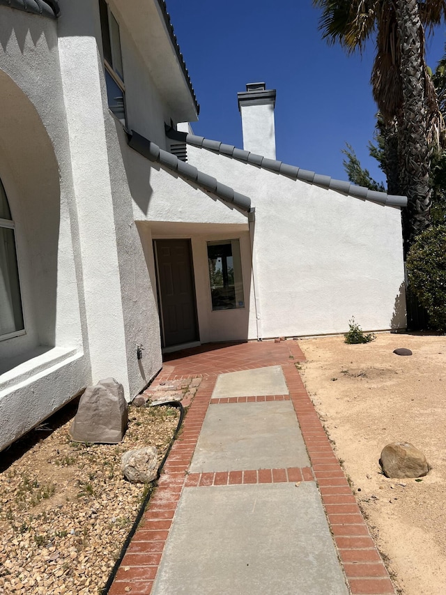 property entrance featuring a tile roof, stucco siding, a patio, and a chimney