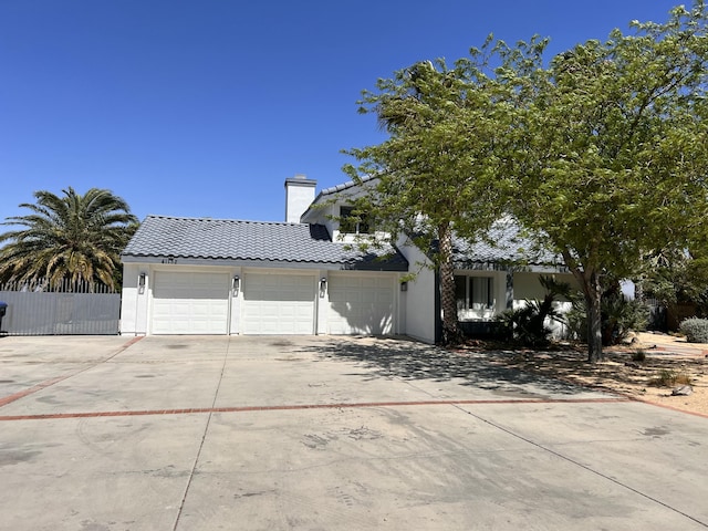 view of front of home featuring a tiled roof, fence, an attached garage, a chimney, and concrete driveway
