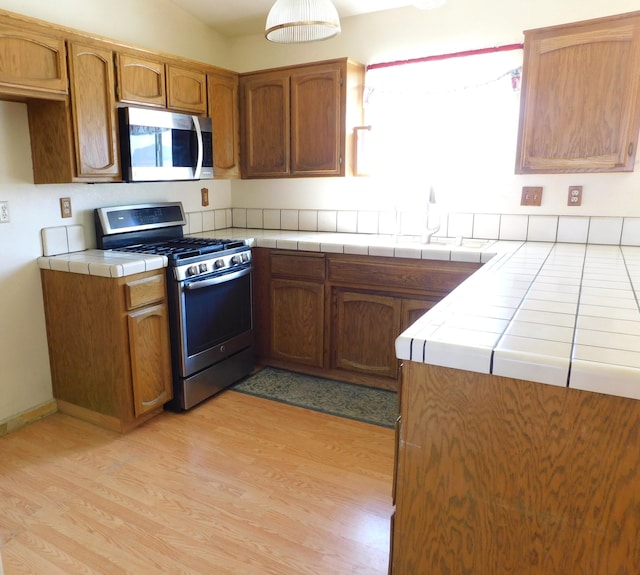 kitchen with sink, vaulted ceiling, light hardwood / wood-style flooring, tile counters, and stainless steel appliances