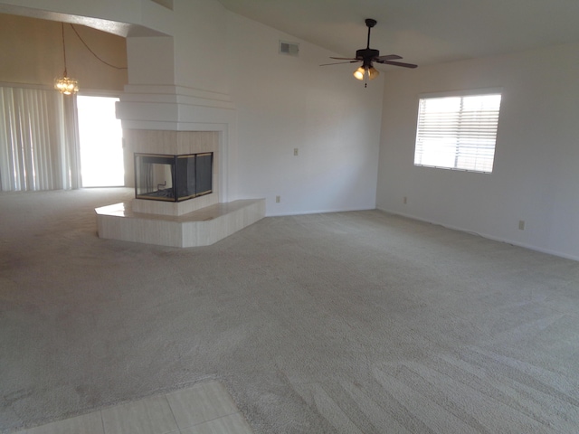 unfurnished living room featuring visible vents, carpet floors, ceiling fan with notable chandelier, a tile fireplace, and high vaulted ceiling