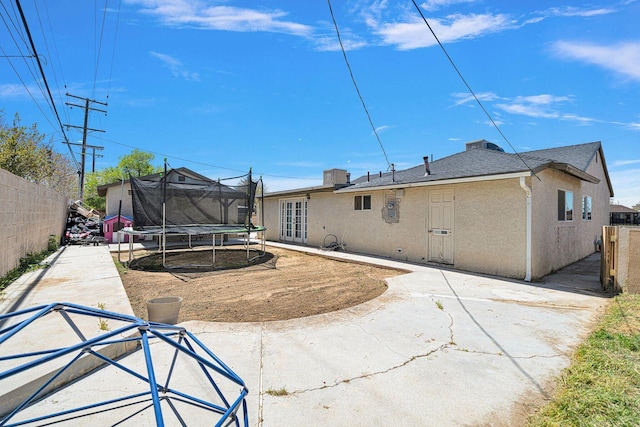 back of property with a patio, a trampoline, fence, and stucco siding