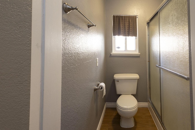 bathroom with a textured wall, toilet, a stall shower, wood finished floors, and baseboards