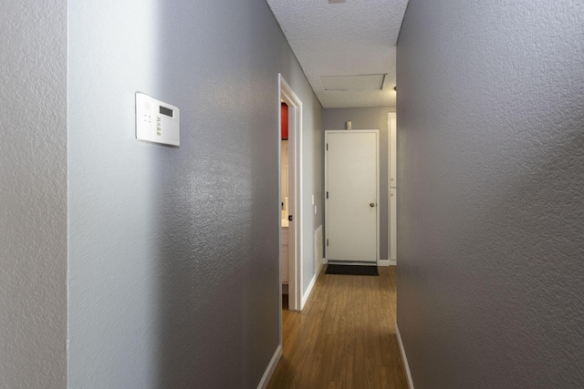 hallway with attic access, a textured wall, and baseboards