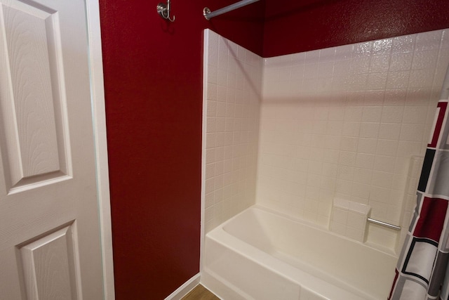 full bath featuring shower / bath combo, a textured wall, and baseboards