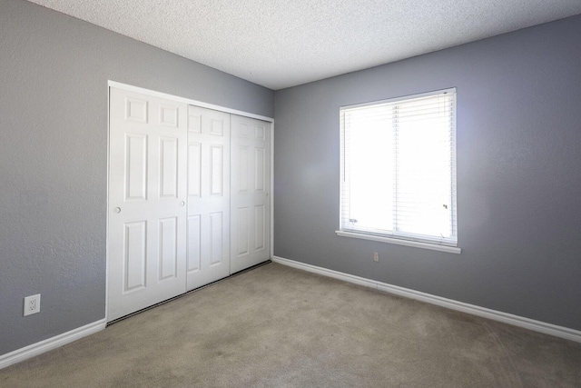 unfurnished bedroom with a closet, light colored carpet, a textured ceiling, and baseboards