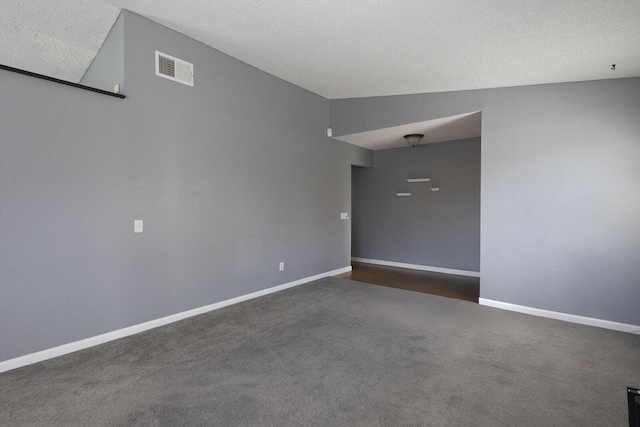 spare room with a textured ceiling, dark carpet, visible vents, and baseboards