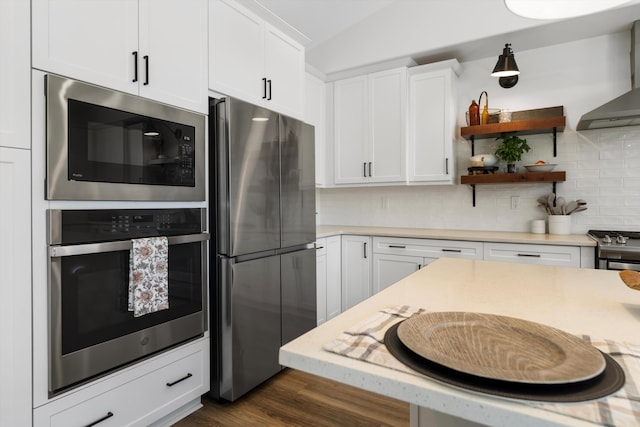 kitchen with appliances with stainless steel finishes, wall chimney exhaust hood, white cabinets, tasteful backsplash, and dark wood finished floors