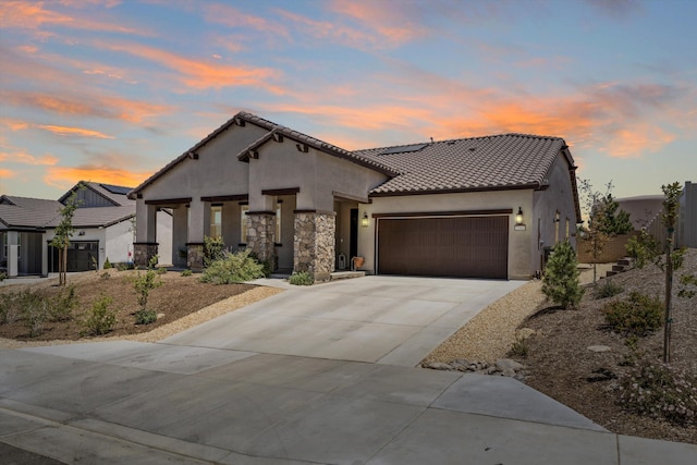 mediterranean / spanish house with stucco siding, an attached garage, driveway, a tiled roof, and roof mounted solar panels