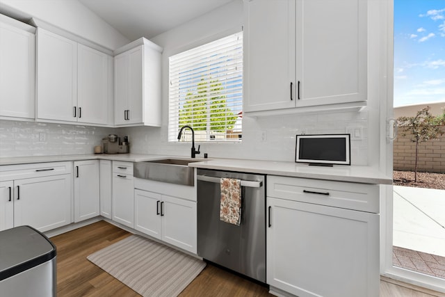 kitchen with stainless steel dishwasher, a sink, tasteful backsplash, white cabinetry, and light countertops