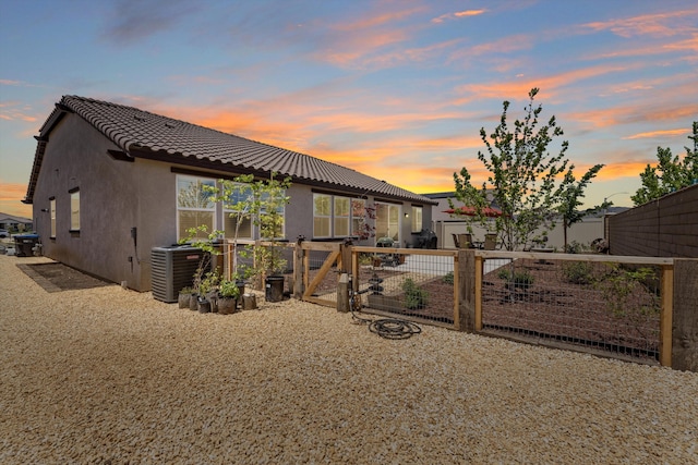 back of property at dusk with stucco siding, a gate, a tile roof, and fence