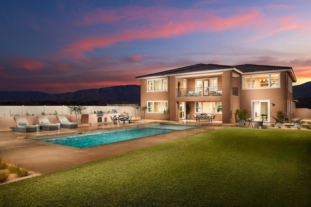 back house at dusk featuring a lawn, a mountain view, a balcony, a fenced in pool, and a patio