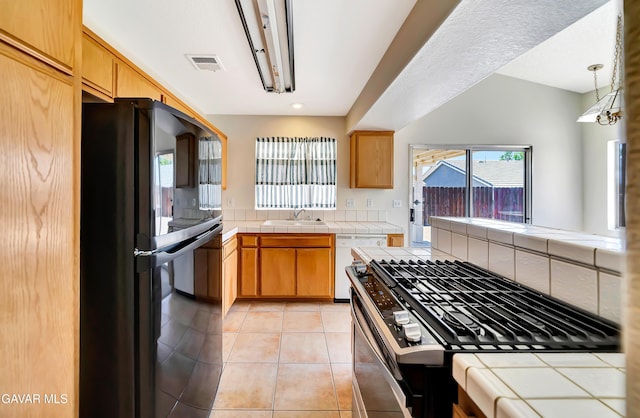 3524 San Jacinto Ave, Rosamond, CA 93560 - kitchen with freestanding refrigerator, stainless steel range with gas cooktop, tile countertops, white dishwasher, and light tile patterned floors