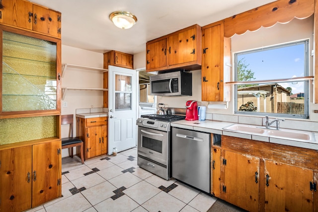 kitchen featuring a sink, open shelves, brown cabinets, light countertops, and appliances with stainless steel finishes