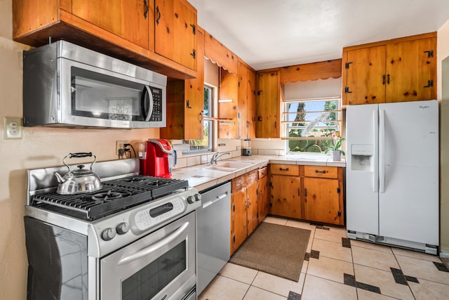kitchen featuring a sink, brown cabinetry, light tile patterned floors, and appliances with stainless steel finishes