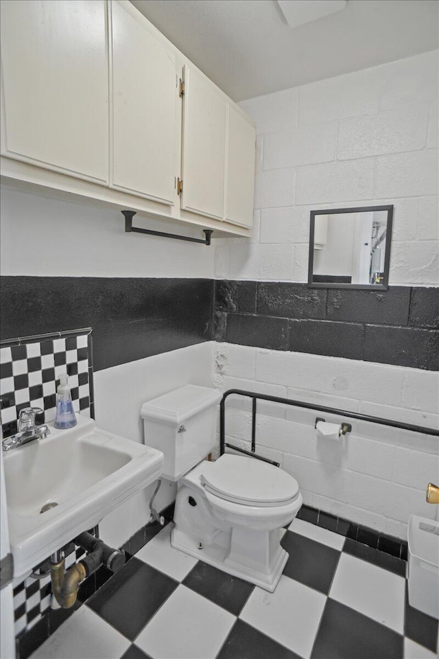 half bathroom featuring toilet, tasteful backsplash, a sink, and tile patterned floors