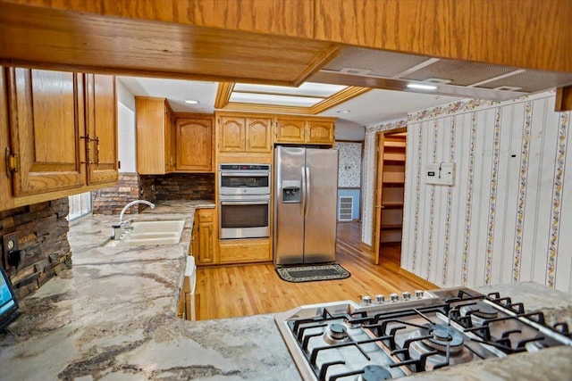 kitchen with light stone counters, light wood finished floors, decorative backsplash, appliances with stainless steel finishes, and a sink