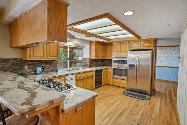 kitchen featuring appliances with stainless steel finishes, brown cabinetry, a peninsula, and light wood finished floors