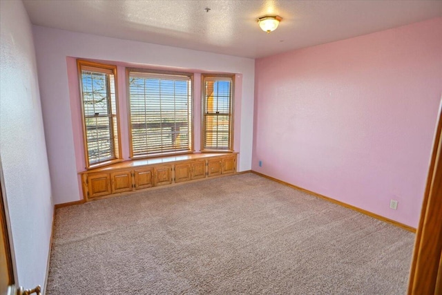 unfurnished room featuring light colored carpet, a textured ceiling, and baseboards