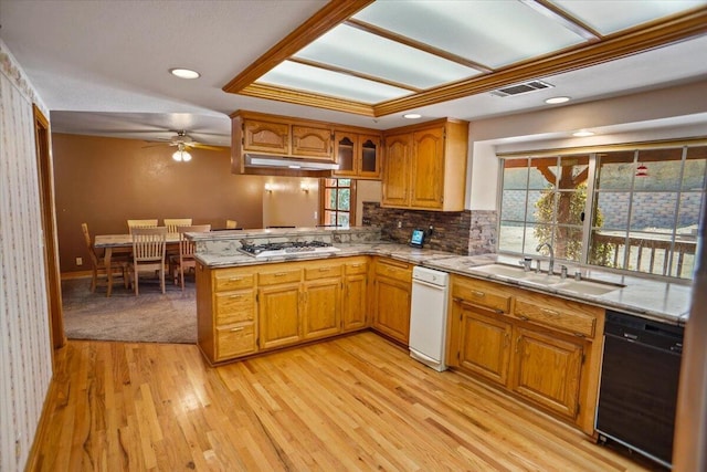 kitchen with black dishwasher, light wood finished floors, brown cabinetry, a sink, and a peninsula