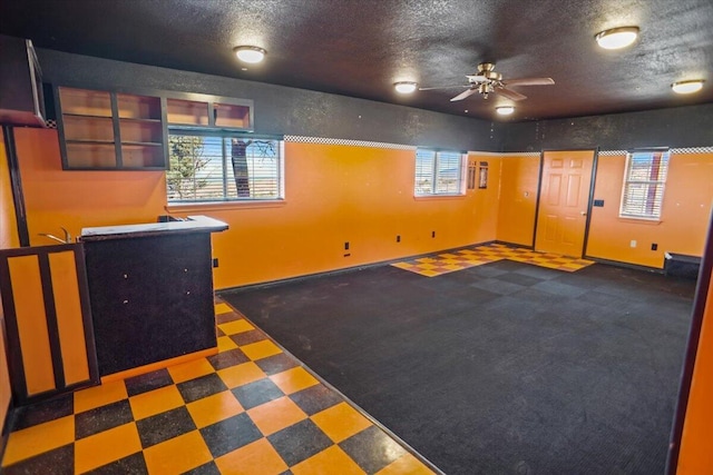 interior space featuring ceiling fan, a textured ceiling, baseboards, and tile patterned floors