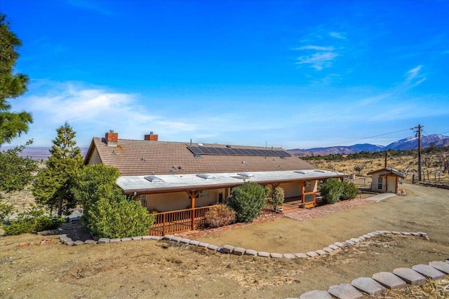 rear view of house with covered porch, a chimney, a mountain view, and solar panels