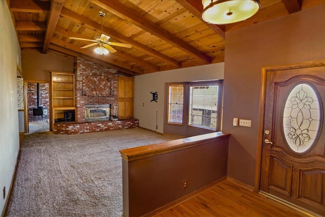 entryway featuring a ceiling fan, wooden ceiling, wood finished floors, vaulted ceiling with beams, and a brick fireplace