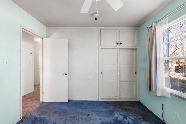 unfurnished bedroom with ceiling fan, a closet, and dark colored carpet