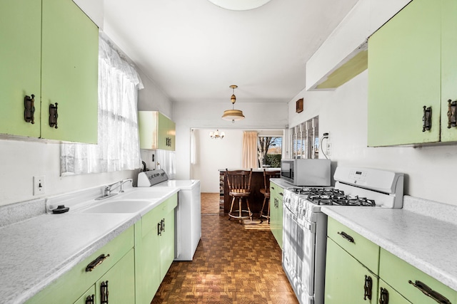 kitchen featuring dark parquet flooring, hanging light fixtures, white range with gas cooktop, washer / dryer, and sink