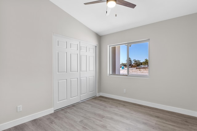 unfurnished bedroom with lofted ceiling, a closet, ceiling fan, and light wood-type flooring