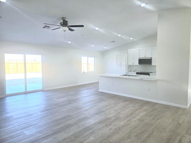 unfurnished living room featuring ceiling fan, sink, a wealth of natural light, and light wood-type flooring