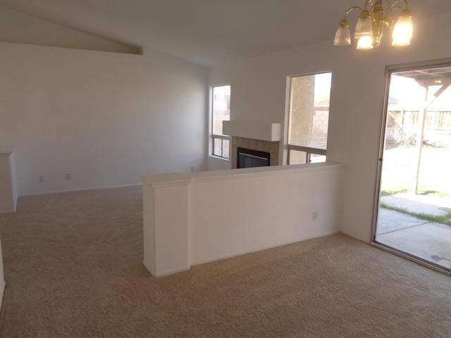 interior space featuring a tile fireplace, a notable chandelier, carpet flooring, vaulted ceiling, and decorative light fixtures