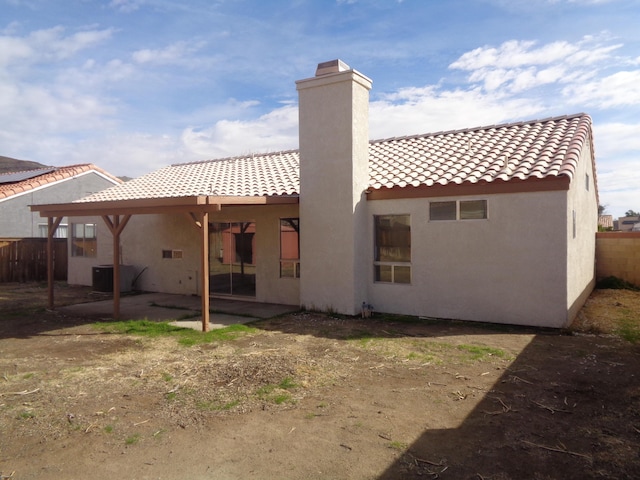 rear view of house with a tiled roof, a chimney, a patio, and stucco siding