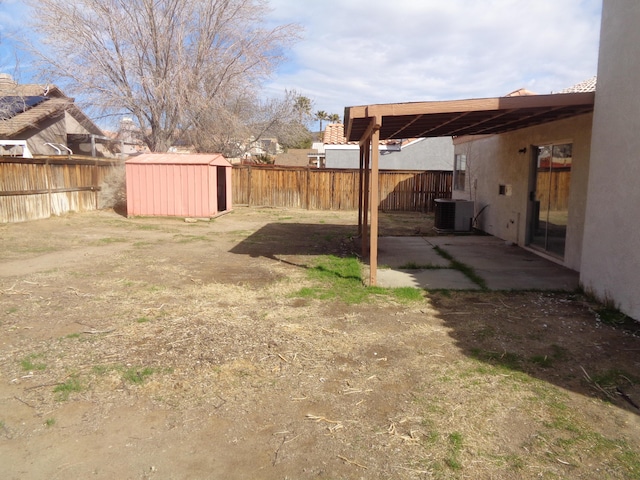 view of yard with central AC unit, a fenced backyard, a storage unit, and an outbuilding