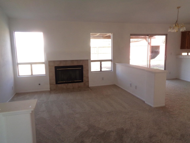 unfurnished living room featuring baseboards, light colored carpet, a tiled fireplace, and an inviting chandelier