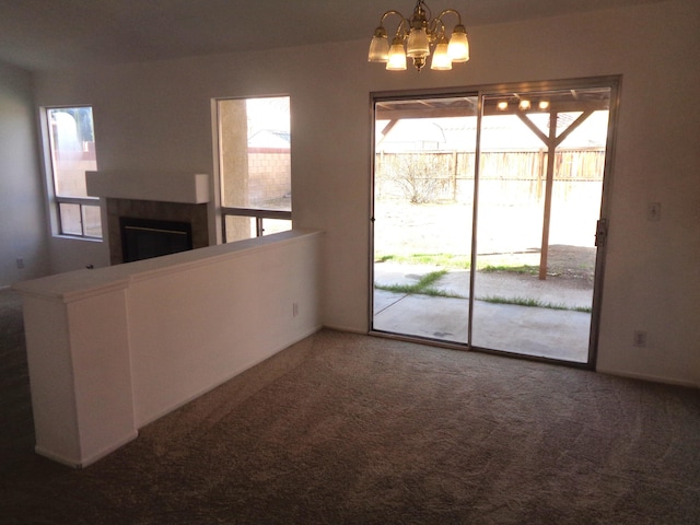 carpeted empty room featuring an inviting chandelier, a wealth of natural light, and a tile fireplace