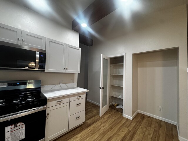 kitchen featuring stainless steel microwave, range, light wood-style flooring, baseboards, and light stone countertops