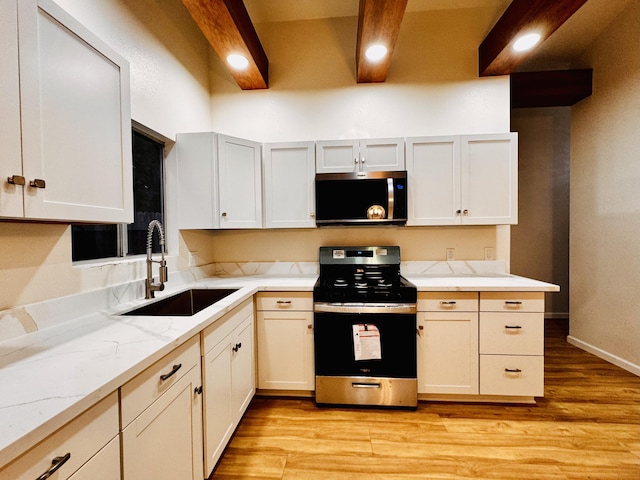 kitchen featuring stainless steel appliances, a sink, light stone countertops, light wood finished floors, and white cabinets