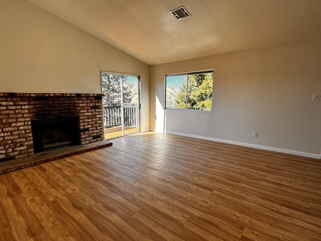 unfurnished living room with lofted ceiling, wood finished floors, baseboards, and a brick fireplace