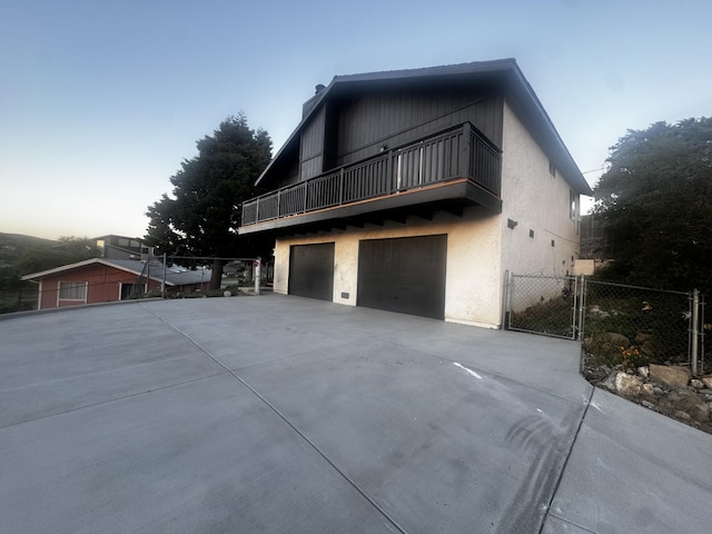 view of property exterior with a balcony, driveway, a garage, fence, and a gate